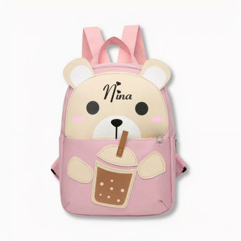 IMG_sac_dos_perso_motif_lapin_presentation.jpeg Kleiner rosa Rucksack für Kinder in Form eines Teddybären, der mit einem Strohhalm an einem Glas nippt, auf dem der Name Nina steht, auf hellgrauem Hintergrund