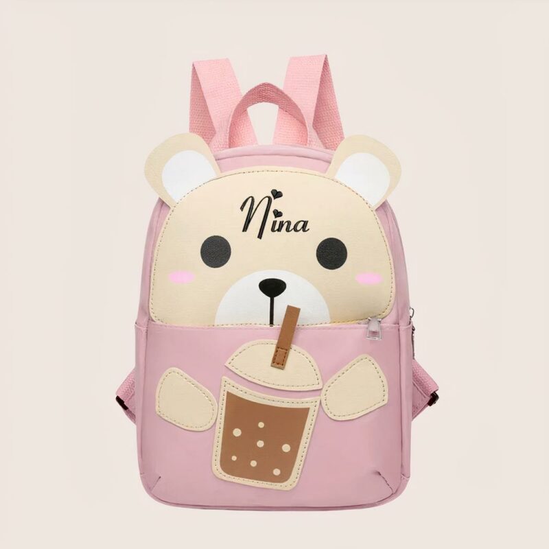 Kleiner rosa Rucksack für Kinder in Form eines Teddybären, der mit einem Strohhalm an einem Glas nippt, auf dem der Name Nina steht, auf einem malvenfarbenen Hintergrund.