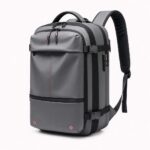 Un sac à dos voyage homme compression sous vide avec pompe gris, avec plusieurs fermetures éclair, des sangles de compression et une poignée sur le dessus, sur fond blanc.
